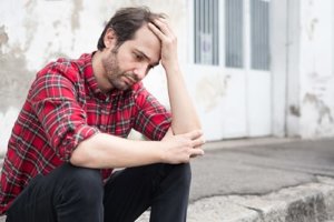 A man sits on a curb wondering if he needs treatment for heroin addiction