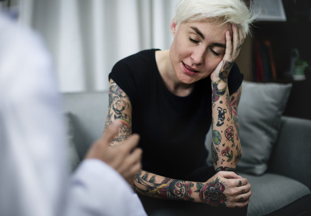 Depressed woman having a counseling session tattooed woman sits on couch talking to counselor about heroin withdrawal symptoms